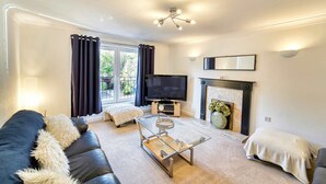 A modern living room with a black leather sofa, a glass coffee table, a flat-screen TV, a fireplace, and a large window with curtains. - Host Stay Lion Court (Worcester)