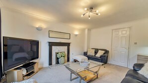A modern living room with a flat-screen TV, a fireplace, a glass coffee table, a sofa, and a door. - Host Stay Lion Court (Worcester)