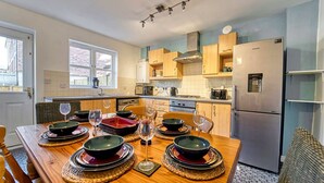 A modern kitchen with wooden cabinets, a stainless steel refrigerator, and a dining table set for four with glassware. - Host Stay Lion Court (Worcester)