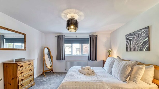 A bedroom with a bed, a dresser, a mirror, a radiator, a window with curtains, and a ceiling light fixture. - Host Stay Lion Court (Worcester)