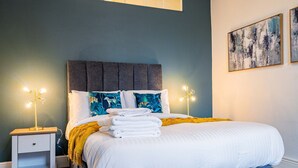 Un letto rifatto con lenzuola bianche e una coperta azzurra, un comodino con una lampada, e una parete con due opere d'arte incorniciate.