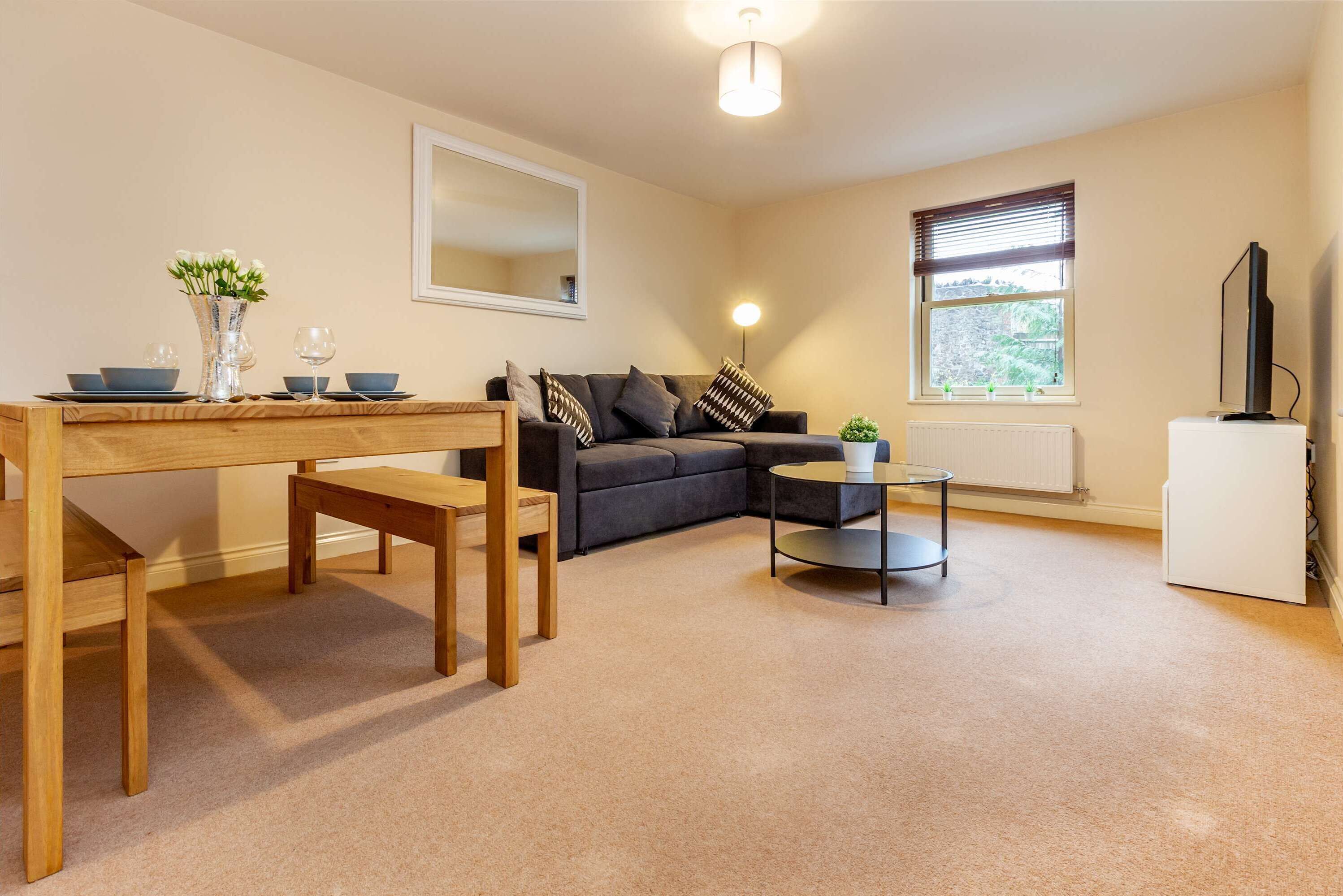 A living room with a wooden dining table, a grey sofa, a small round table, and a white radiator.