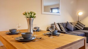 A dining table set with bowls, wine glasses, and cutlery, a vase with flowers, and a sofa with cushions in a modern living room. - Host Stay Hillbrook House Apartment (Malvern)