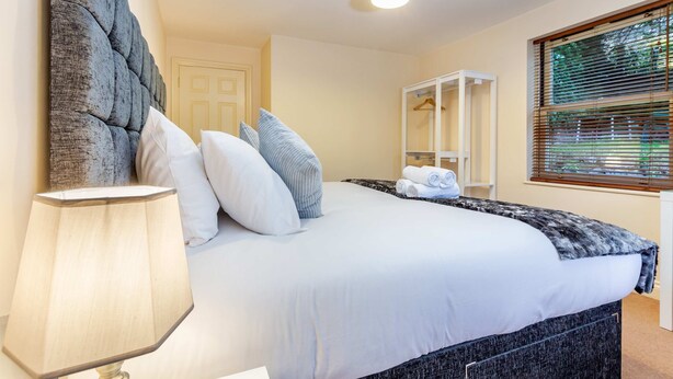 A bedroom with a large bed, a bedside table with a lamp, a wardrobe, and a window with blinds. - Host Stay Hillbrook House Apartment (Malvern)