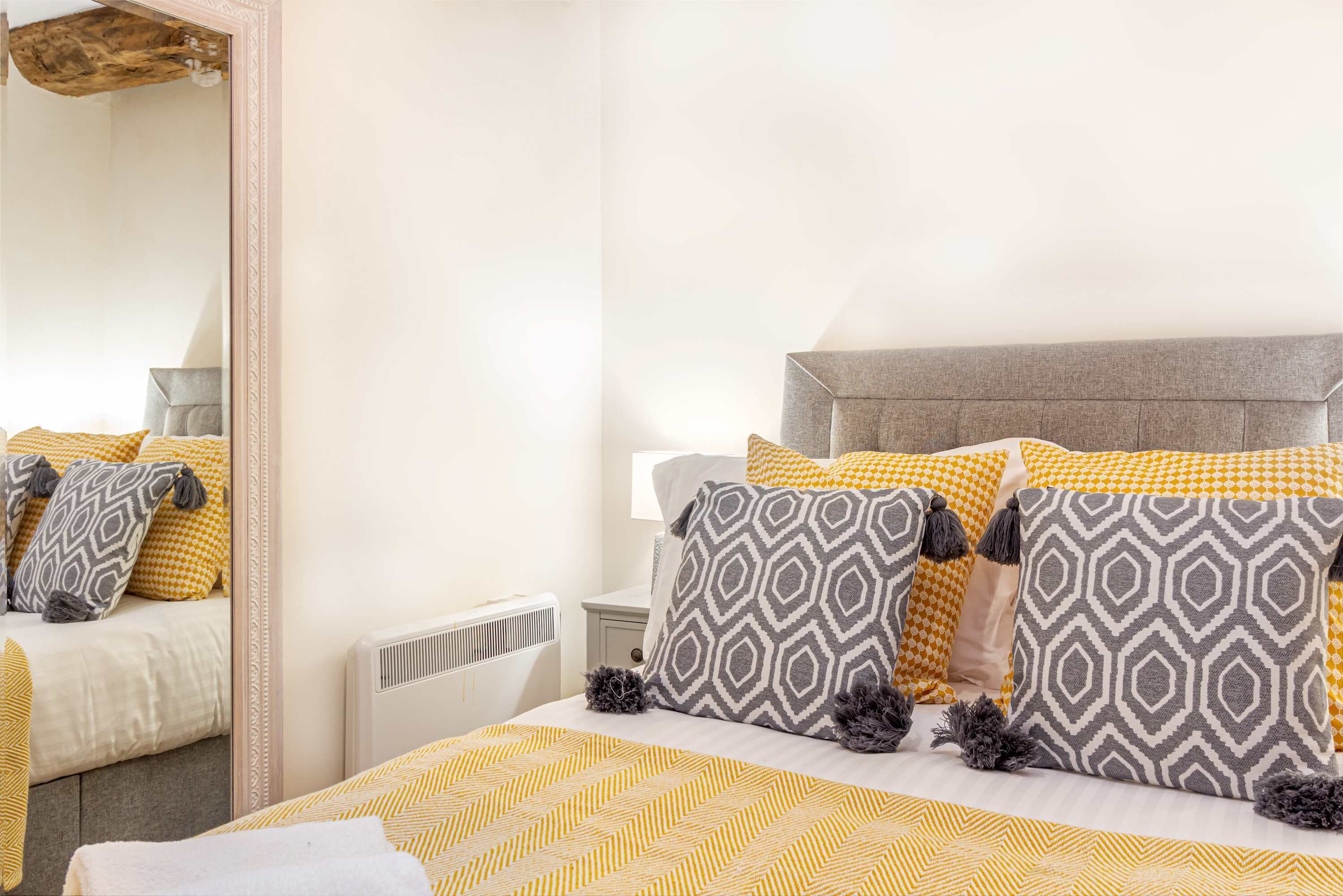 A neatly arranged bedroom with a bed, pillows, a bedside table, and a mirror.
