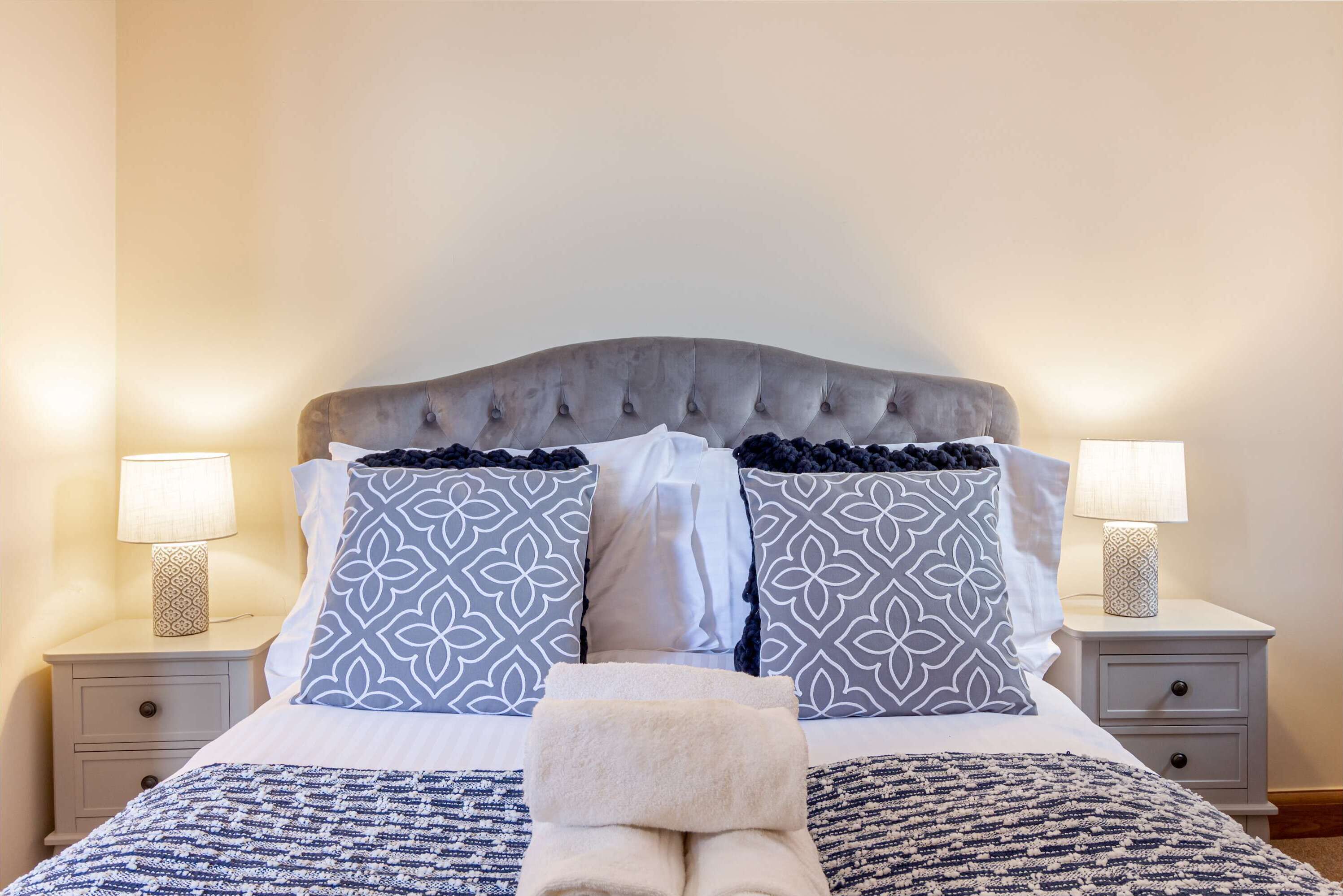 A neatly made bed with patterned pillows, a folded towel, and two bedside lamps on nightstands.