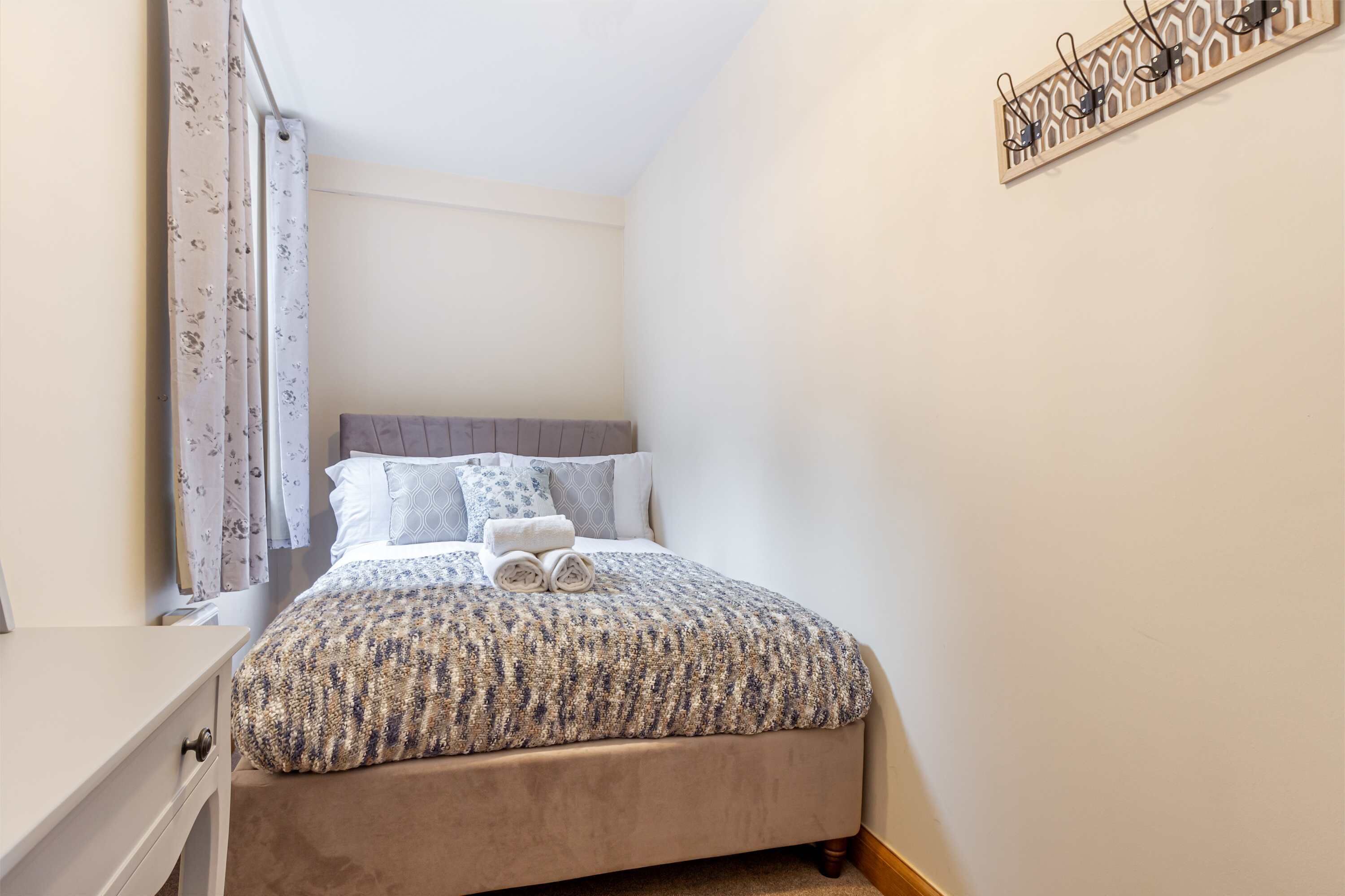 A neatly made bed with a patterned bedspread and pillows, a bedside table, and a wall-mounted light fixture.