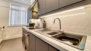 A modern kitchen with two sinks, a window with blinds, and a countertop with a coffee maker. - Host Stay The Bell (Stourbridge)