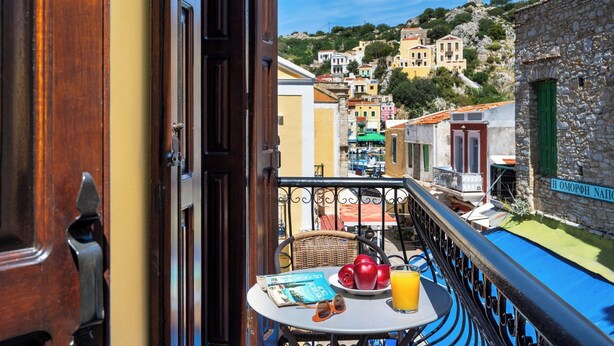En balkon med et bord, en fletstol, en bog, æbler og et glas appelsinjuice.