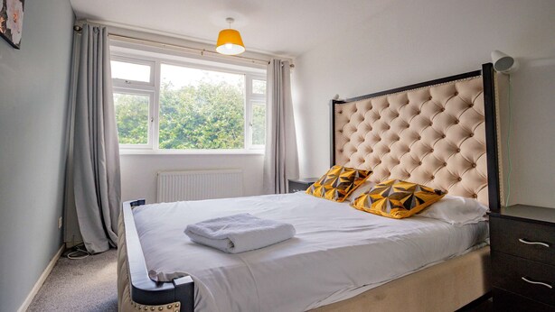 Een net opgemaakt bed met een witte deken, een gestoffeerd hoofdbord en twee kussens met dessin.