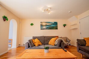 Una sala de estar con un sofá gris, una mesa de centro de madera y un cuadro de un paisaje.