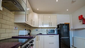 Een keuken met witte kasten, een magnetron, een koelkast en een gasfornuis.