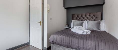 Un dormitorio con una cama grande, cabecera oscura, mesita de noche y una puerta blanca.
