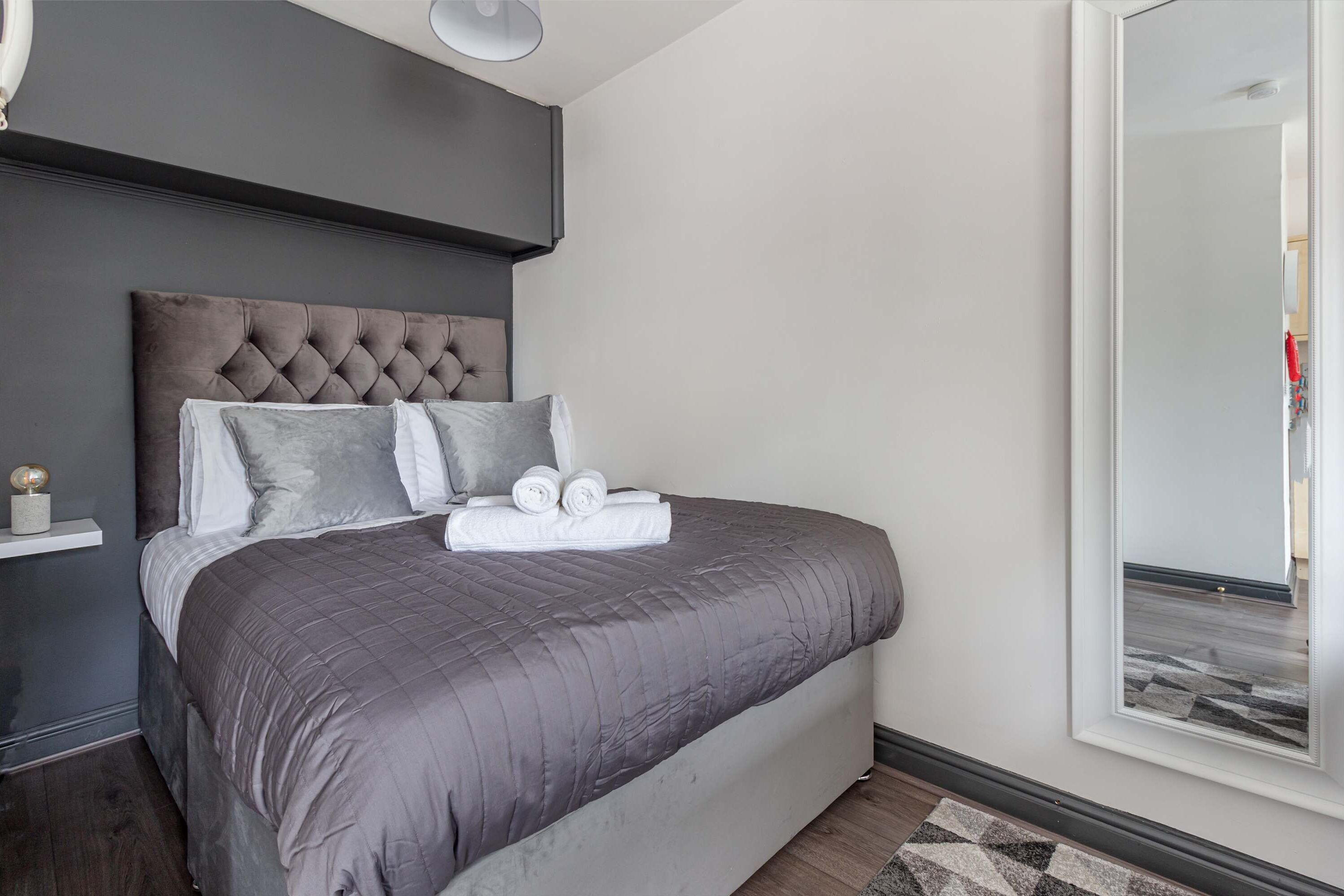 Ein modernes Schlafzimmer mit einem gesteppten Kopfteil, einem großen Bett mit grauer Bettwäsche und einem Spiegel an der Wand.