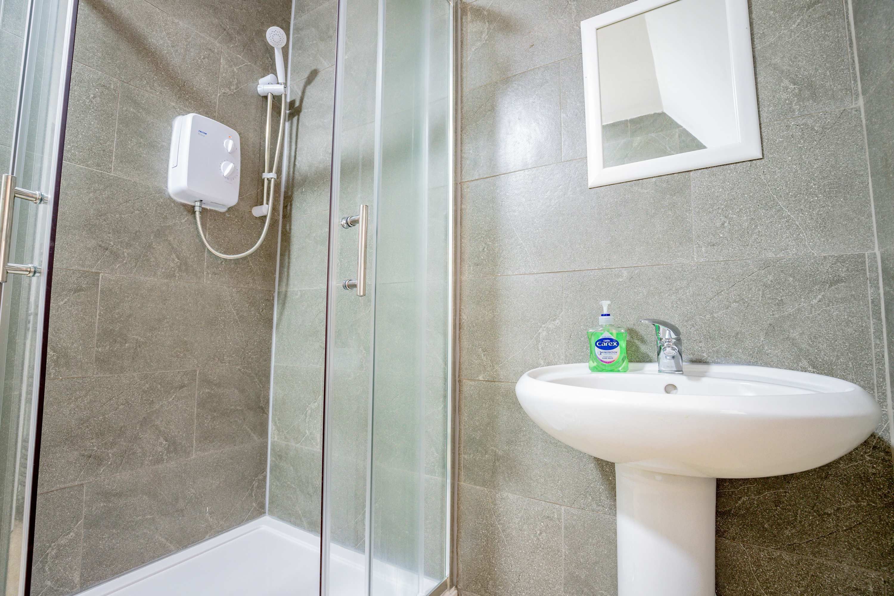 A bathroom with a glass-enclosed shower, a white pedestal sink, and a mirror above the sink.