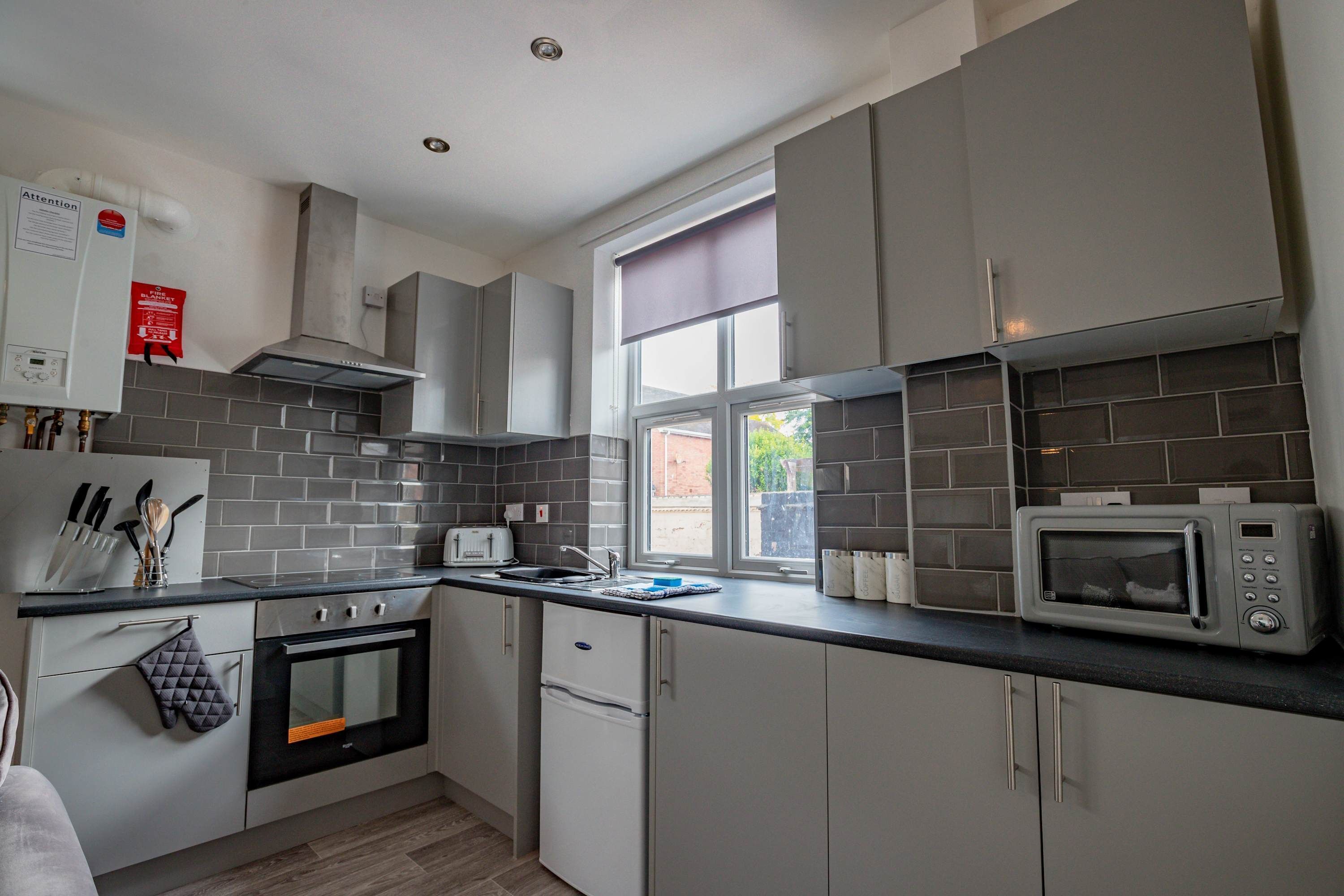 A modern kitchen with grey cabinets, a built-in oven, a microwave, and a window with a view.