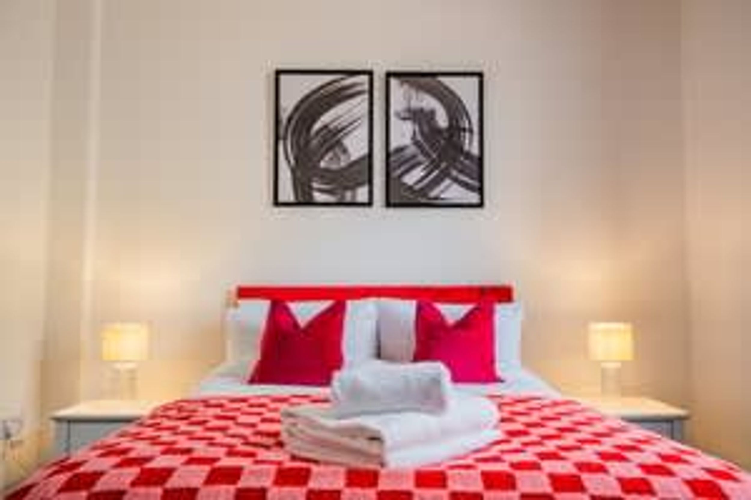 Une chambre d’hôtel avec une couvre-lit à carreaux, des oreillers rouges et blancs, et une œuvre d’art abstraite accrochée au mur.