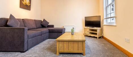 A living room with a sectional sofa, a wooden coffee table, a television, and a window with a view.
