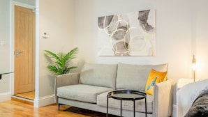 Ein Wohnzimmer mit grauem Sofa, einem kleinen runden Tisch, einem Blumentopf und einem Wandbild.