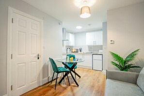 En kompakt opholdsstue med spiseplads, tekøkken og sofa.