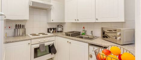 A kitchen with white cabinets, a stove, a sink, and a toaster.
