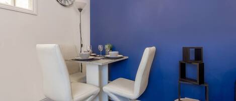 A dining area with a white table and chairs, a clock on the wall, and a blue accent wall.