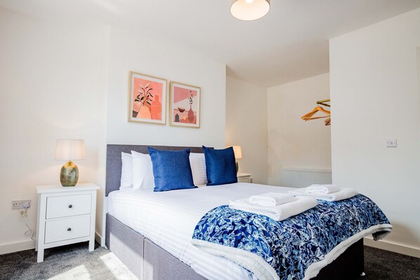 A neatly made bed with blue and white bedding, a white nightstand with a lamp, and two framed artworks on the wall. - Host Stay Bromyard Flat 1 (Worcester)