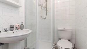Une salle de bain avec un lavabo blanc, des toilettes et une douche fermée par des parois en verre.