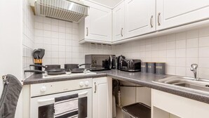 Une cuisine de taille réduite avec des meubles blancs, une cuisinière, un évier et une machine à café.