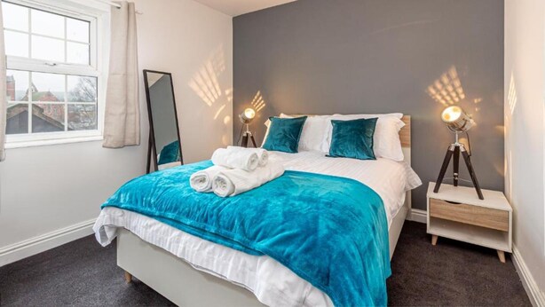 Une chambre à coucher bien rangée, avec un lit, deux lampes de chevet, une table de chevet et une fenêtre avec des rideaux.