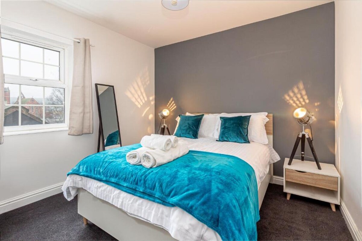A neatly arranged bedroom with a bed, two bedside lamps, a bedside table, and a window with curtains.