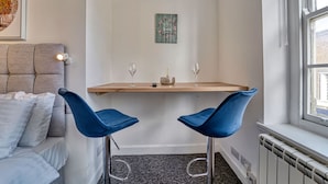 Ein Eckzimmer mit Bett, einem kleinen Tisch mit zwei Stühlen, einer Wanddekoration und einem Fenster.