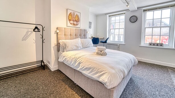 Ein Schlafzimmer mit Bett, Heizkörper, Fenster mit Blick und einer Uhr an der Wand.