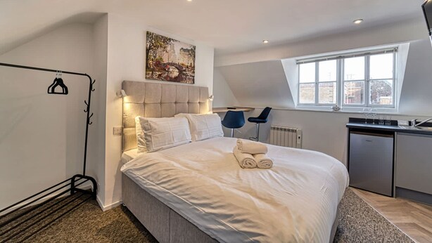Une chambre moderne avec un grand lit, une tête de lit, un tableau, un bureau et une fenêtre.
