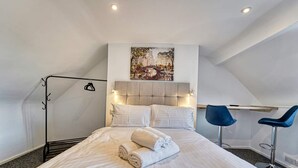 Une chambre à coucher avec un lit, une tête de lit, deux chaises, un tableau et un luminaire au plafond.