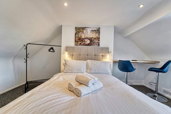 Une chambre à coucher avec un lit, une tête de lit, deux chaises, un tableau et un luminaire au plafond.