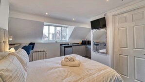 Une chambre avec un lit, une fenêtre, une petite kitchenette et une porte.