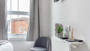 A modern bedroom with a bed, a desk with a plant, and a view of a brick building through a window. - Host Stay The Bull Inn Flat 1 (Worcester)