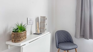 A white console table with a woven plant holder, a small vase, and a candle holder. A grey upholstered chair is positioned to the right. - Host Stay The Bull Inn Flat 2 (Worcester)