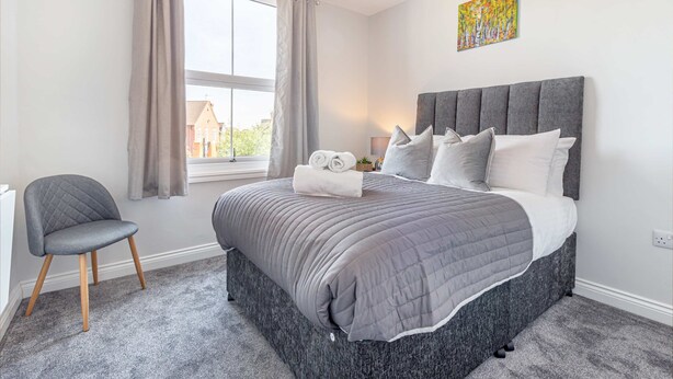 A bedroom with a large bed, a chair, a window with curtains, and a painting on the wall. - Host Stay The Bull Inn Flat 2 (Worcester)