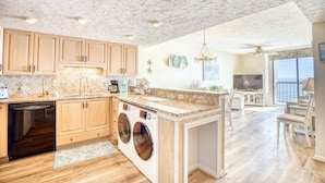 A modern kitchen with wooden cabinets, a dishwasher, and a built-in washer and dryer. - Waterpointe II 705 | Oceanfront 3 Bedroom Condo (North Myrtle Beach)