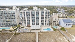 A high-rise residential building with multiple balconies, a rooftop pool, and a pedestrian bridge. - Waterpointe II 705 | Oceanfront 3 Bedroom Condo (North Myrtle Beach)