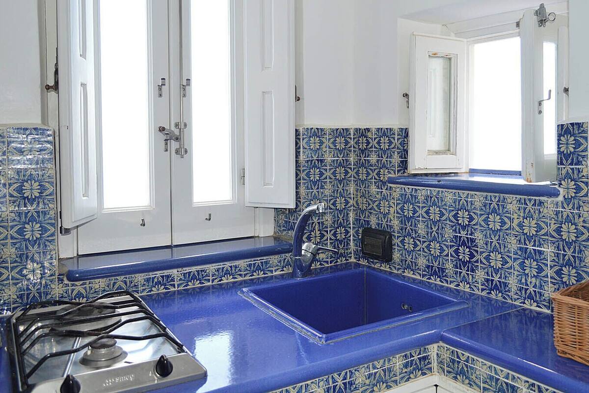 A kitchen with blue and white tiles, a gas stove, and a sink.