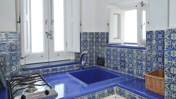 A kitchen with blue and white tiles, a gas stove, and a sink. - Villa Il Galeone (Lipari)