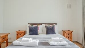 Ein ordentlich bezogenes Bett mit Kissen und Decke, zwei Nachttische und ein Nachttisch aus Holz.