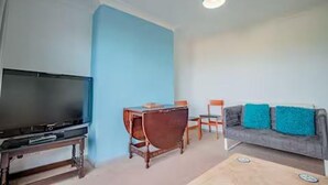 Ein Wohnzimmer mit Fernseher, einem Holztisch, einer blauen Sofaausstattung und einer türkisfarbenen Deckenleuchte.
