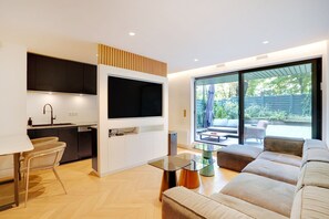 A modern kitchen with a flat-screen TV, a dining area with a table and chairs, and a large sofa in a bright living room with a sliding glass door to a patio. - Chic Apt With Garden - 1bd/2p - Neuilly-sur-seine (Neuilly-sur-Seine)