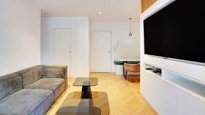 A modern living room with a sectional sofa, a glass coffee table, a flat-screen TV, and a dining area with a table and chairs. - Chic Apt With Garden - 1bd/2p - Neuilly-sur-seine (Neuilly-sur-Seine)