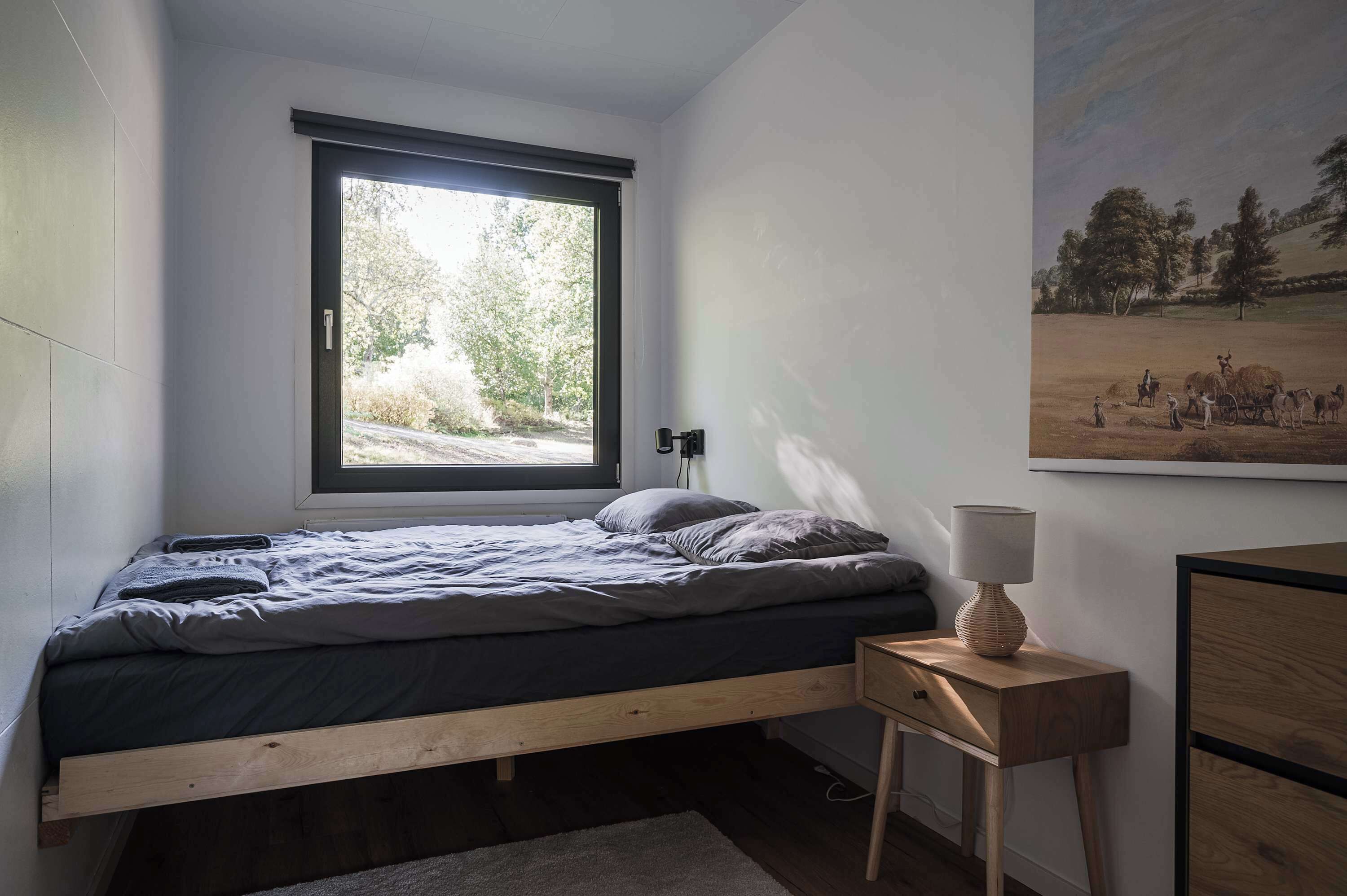 Una camera da letto con un letto singolo, una finestra, un comodino con una lampada e un quadro appeso al muro.