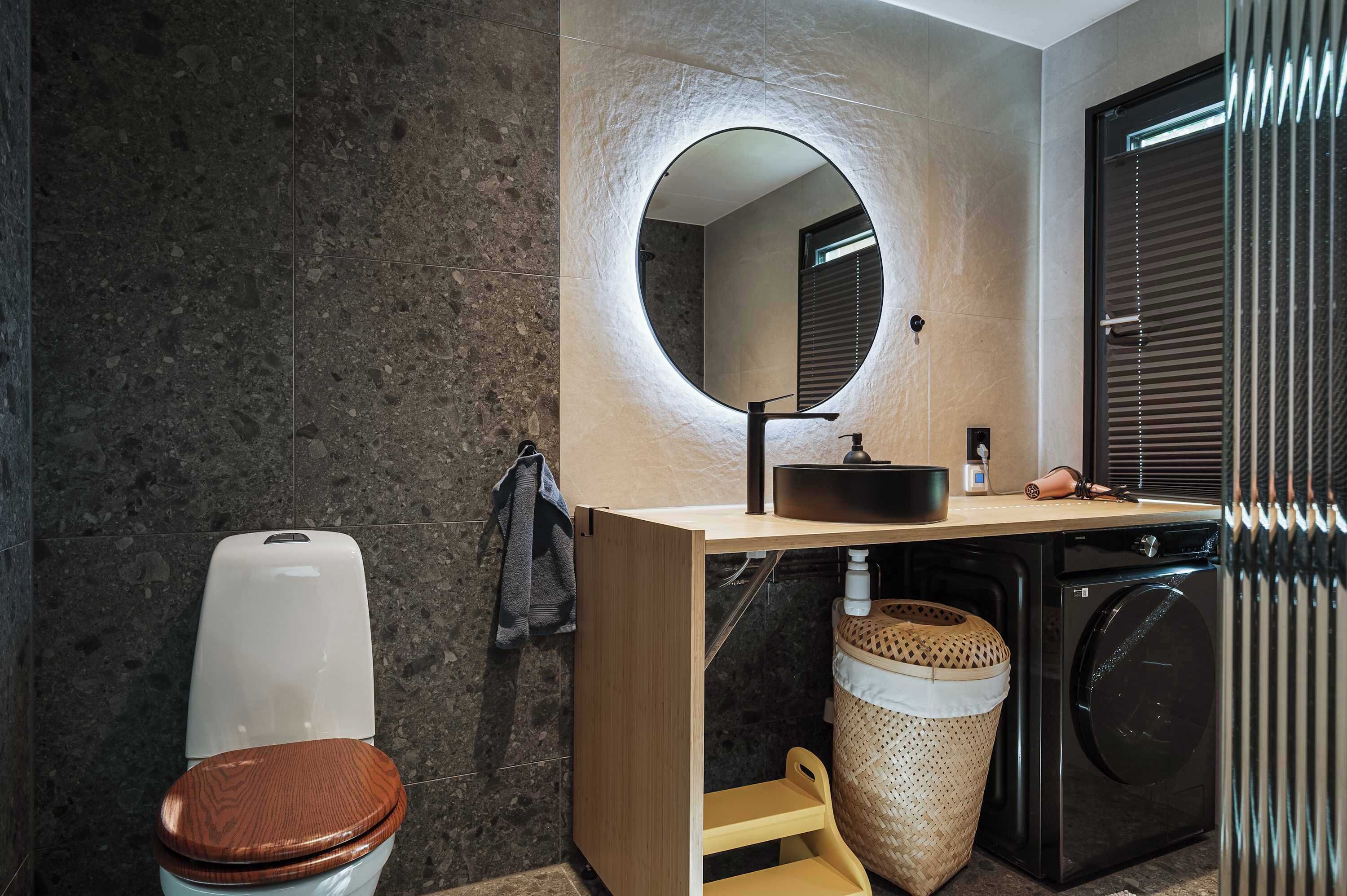 A modern bathroom with a round mirror, a toilet, a sink, and a washing machine.